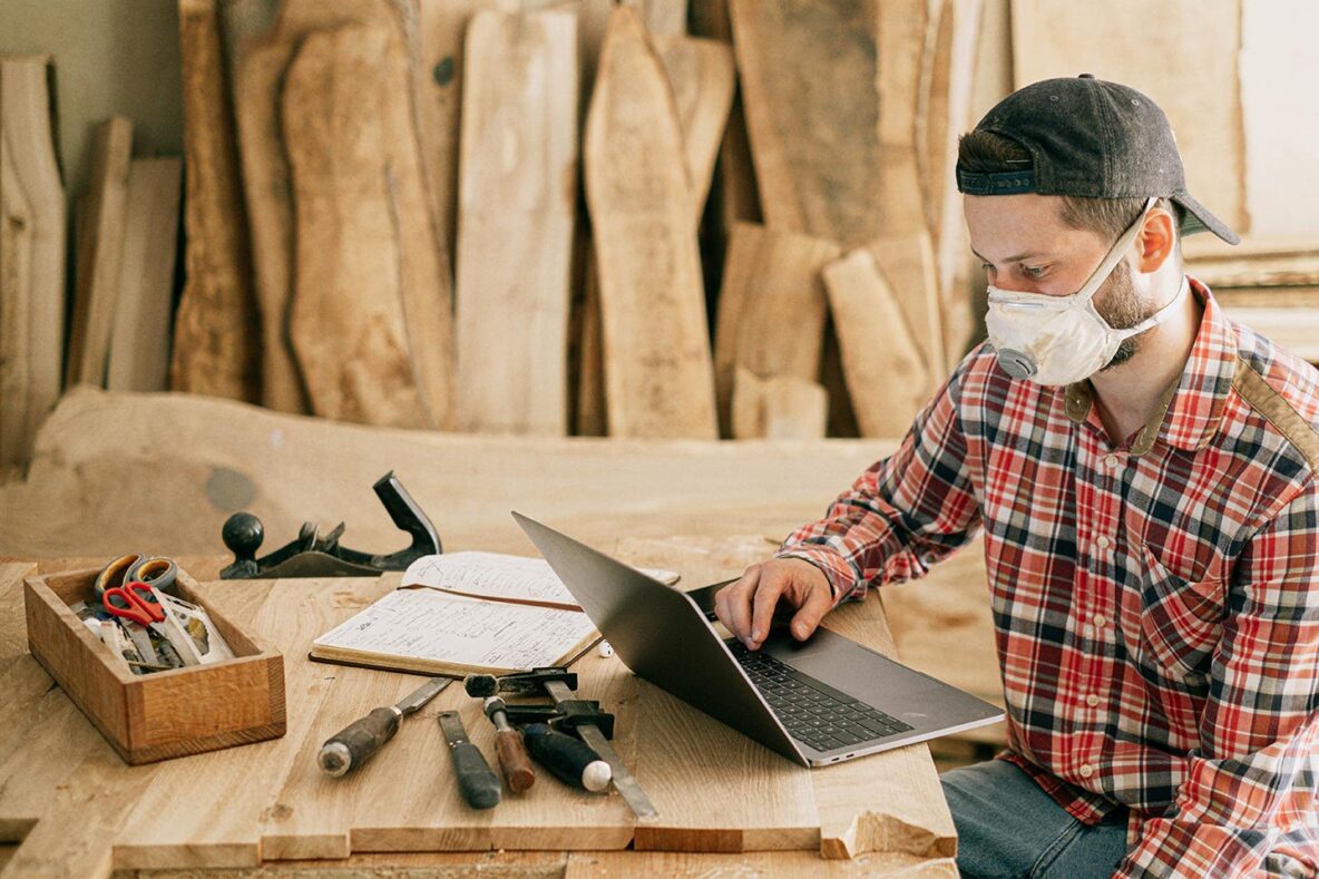 Man in workshop with dust mask on looking at laptop